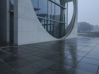 a person walking in the rain in front of an architectural building with windows on either side