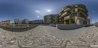 a fish eye photo of some buildings and some stone pathway in the foreground with sun in the sky