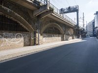 graffiti covered brick wall and gate under an overpass in an urban area with sun light
