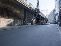 graffiti covered brick wall and gate under an overpass in an urban area with sun light