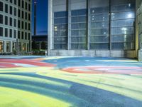 an outside playing surface painted in bright colors at night, surrounded by buildings and lights