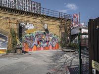 a brick wall with graffiti and an orange gate and fenced in area in front of it