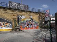 a brick wall with graffiti and an orange gate and fenced in area in front of it