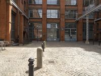 a brick courtyard filled with lots of parking meters and buildings in the background, a building has many windows