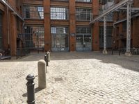 a brick courtyard filled with lots of parking meters and buildings in the background, a building has many windows