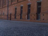 a man riding a skateboard down a cobbled in street next to tall building