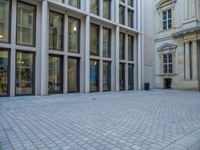 an empty brick courtyard area with two stone columns and two arched windows in the background