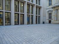 an empty brick courtyard area with two stone columns and two arched windows in the background