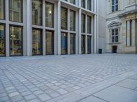 an empty brick courtyard area with two stone columns and two arched windows in the background