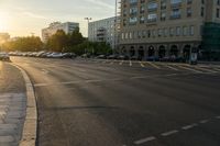 a street is shown with several buildings on both sides of it at sunset, there are many cars parked along side the street