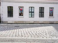 two windows of some sort next to the curb in front of a building on a cobblestone street