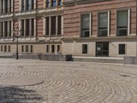 a large stone circular courtyard has many benches outside it, along with a brick sidewalk