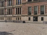 a large stone circular courtyard has many benches outside it, along with a brick sidewalk