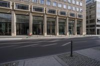 the empty street in front of two tall buildings and a man walking past it through the sidewalk