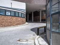 a parking area on the side of a building with tall windows and a bench on the side