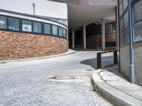 a parking area on the side of a building with tall windows and a bench on the side