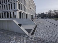 a stone walkway leading into a building in the background has white walls with large windows