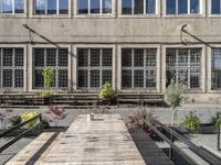 some tables some benches some windows and a building many plants and concrete bricks in a courtyard