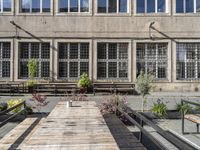 some tables some benches some windows and a building many plants and concrete bricks in a courtyard