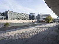 there is a empty walkway outside a building in the evening sun, with a view across the river to large buildings