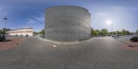 a circular shaped building next to a parking lot with cars driving along it's side