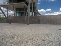 a person on a bike walking through a stone building entrance, in front of an enormous glass wall and stairs