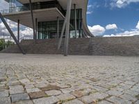 a person on a bike walking through a stone building entrance, in front of an enormous glass wall and stairs