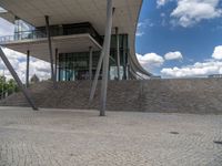 a person on a bike walking through a stone building entrance, in front of an enormous glass wall and stairs