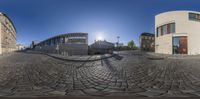 a spherical image of buildings in a city with cobblestone walkways and sun