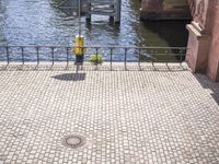 a paved walkway near the water with an umbrella on a pole above it's head