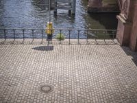 a paved walkway near the water with an umbrella on a pole above it's head