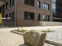 a big boulder outside of a building on a sidewalk near some flowers and street signs