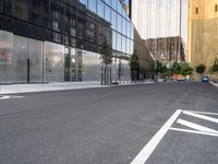 a street lined with parked cars next to large glass buildings near a city sidewalk or walkway