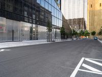 a street lined with parked cars next to large glass buildings near a city sidewalk or walkway