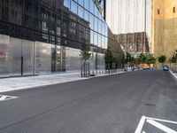 a street lined with parked cars next to large glass buildings near a city sidewalk or walkway