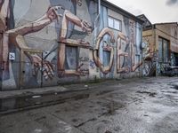 the wall of a building covered with graffiti in a city area that is dirty and has a man on a chair in it