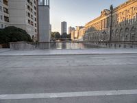 a skateboarder rides along the edge of a paved city street with tall buildings in the background