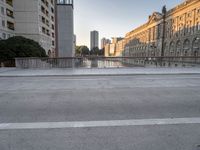 a skateboarder rides along the edge of a paved city street with tall buildings in the background