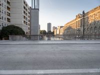 a skateboarder rides along the edge of a paved city street with tall buildings in the background