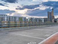 an empty parking lot on top of a concrete floor under cloudy skies over buildings and a highway