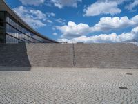 a person on a bike walking through a stone building entrance, in front of an enormous glass wall and stairs