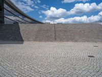 a person on a bike walking through a stone building entrance, in front of an enormous glass wall and stairs