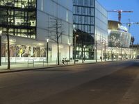 a paved street in the middle of buildings with tall windows at night, with car lights on