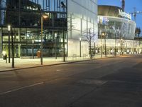 a paved street in the middle of buildings with tall windows at night, with car lights on