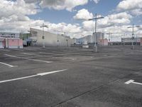 an empty parking lot with a light pole and large warehouse buildings in the background on a cloudy day