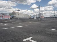 an empty parking lot with a light pole and large warehouse buildings in the background on a cloudy day