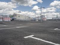 an empty parking lot with a light pole and large warehouse buildings in the background on a cloudy day