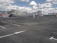 an empty parking lot with a light pole and large warehouse buildings in the background on a cloudy day