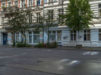 a stop light sits in front of two buildings in the city street, near a parked car and a few bushes