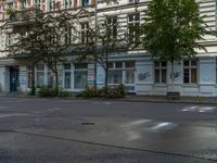 a stop light sits in front of two buildings in the city street, near a parked car and a few bushes